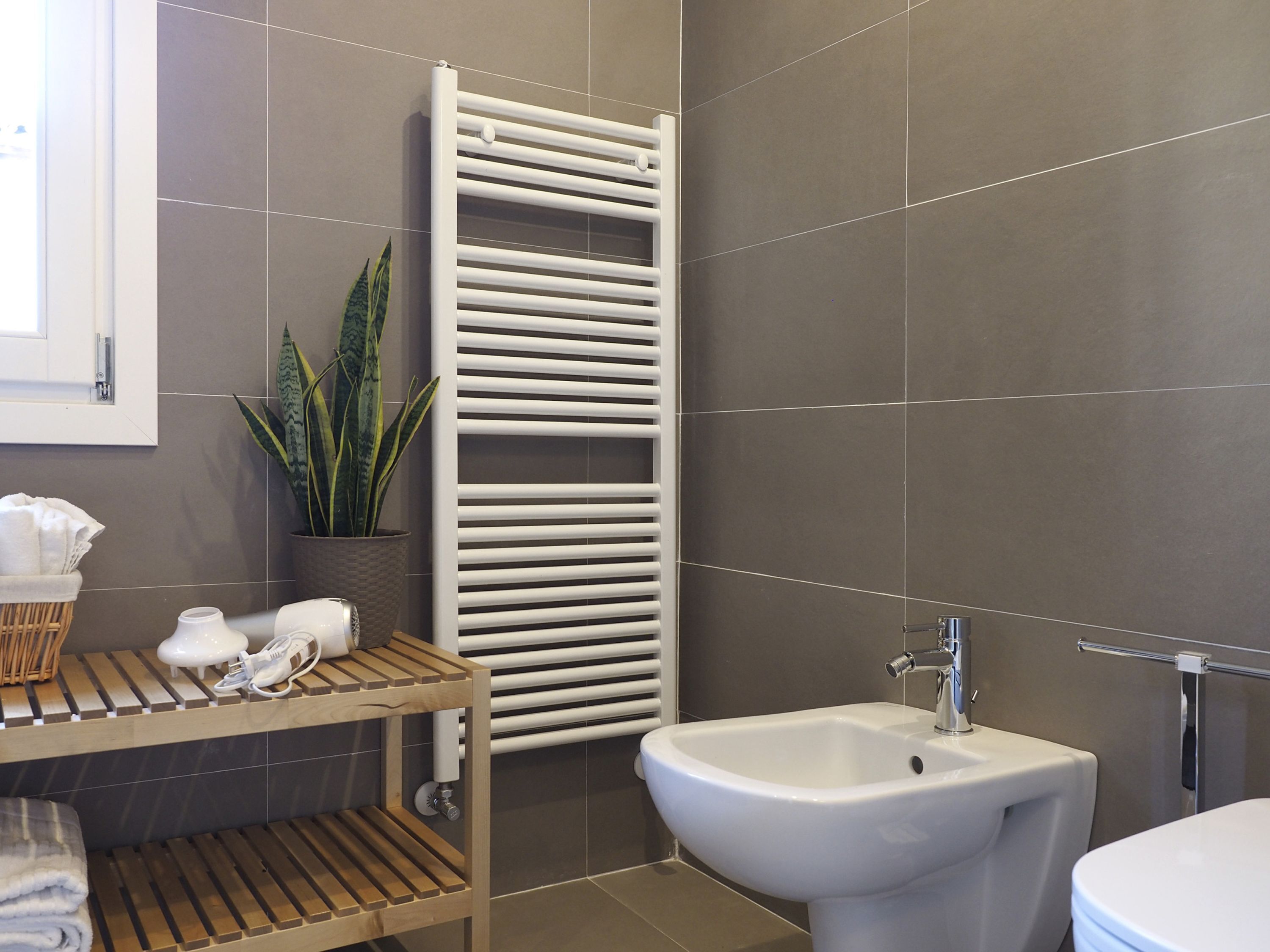 A modern bathroom with a white radiator, a sink, and a shelf with towels and shoes.