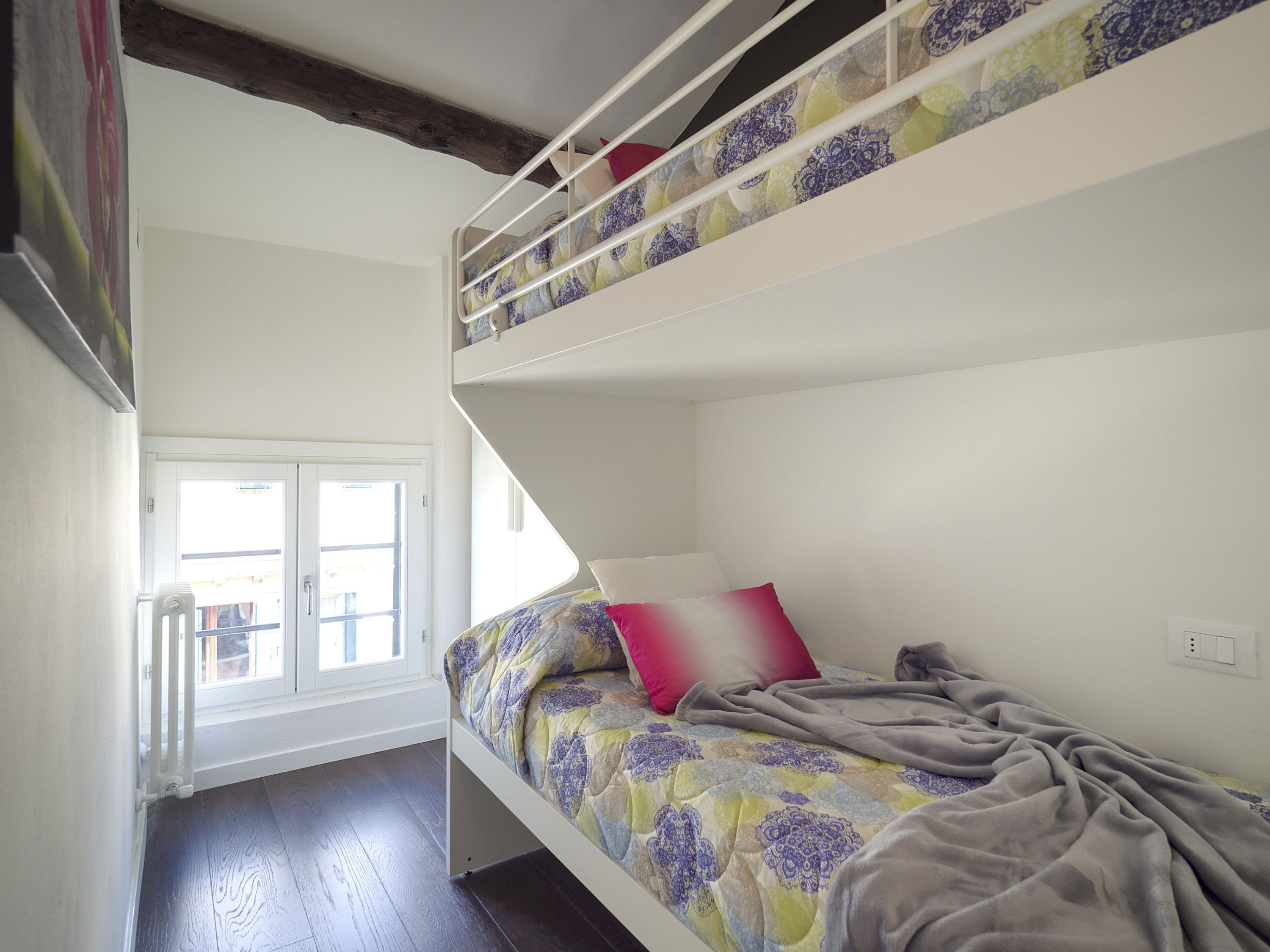 A bunk bed room with a window, white walls, and a wooden floor.