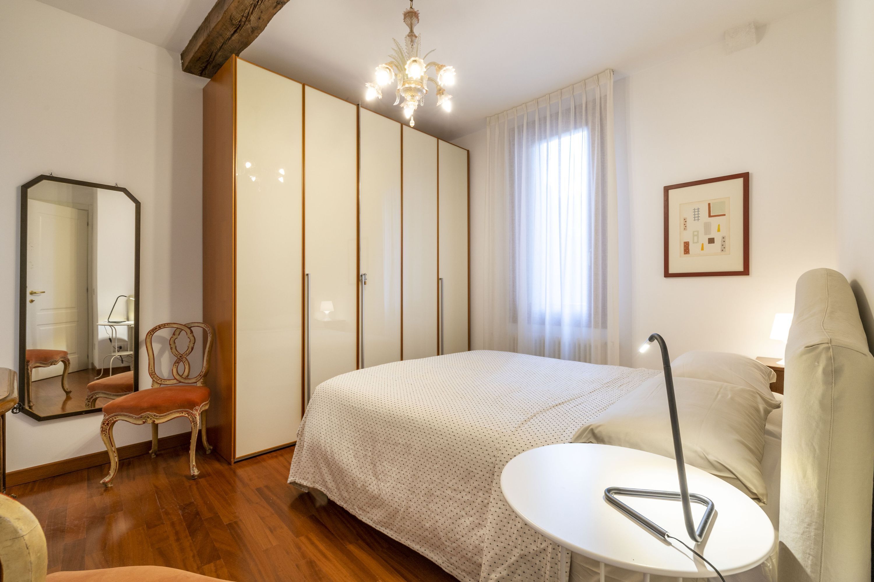 A bedroom with a bed, a chair, a table, a mirror, and a wardrobe.