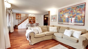 Een woonkamer met een beige modulaire bank, een houten trap en een groot abstract schilderij.