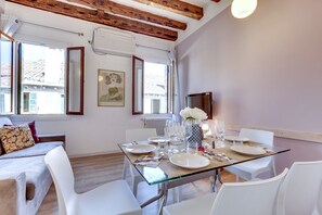 Een eetruimte met een glazen tafel, witte stoelen en een vaas met bloemen.