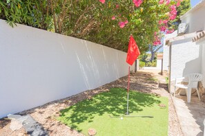 A patio area with a putting green, a red flag, and a white chair.