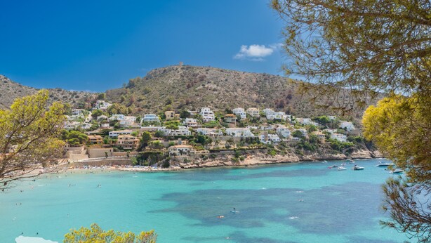 Een kustplaatsje met gebouwen op een heuvel die uitkijken over een turquoise baai.