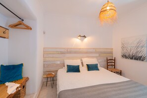 A bedroom with a wooden headboard, a bed with white bedding and teal pillows, a hanging light fixture, and a wall-mounted light.