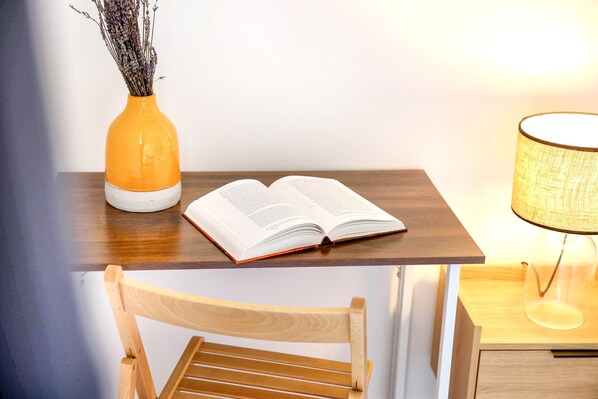 A wooden desk with an open book, a vase with dried flowers, and a lamp.