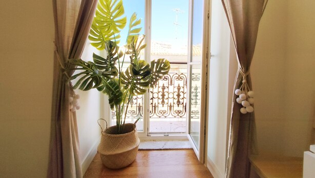 Ein Zimmer mit einem großen Fenster, einem Blumentopf und Blick auf einen Balkon.