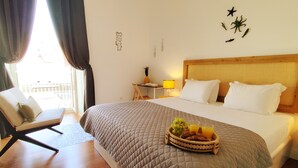 Ein Hotelzimmer mit einem großen Bett, einem Sessel, einem kleinen Tisch mit Lampe und Blick ins Freie.