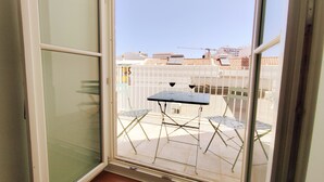 Ein Balkon mit Tisch und Stühlen, eine Glastür und im Hintergrund der Blick auf Gebäude und einen Kran.