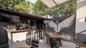Un patio al aire libre con mesas y sillas de madera, una barra con ventilador y un mural con la palabra 'casa' en la pared.