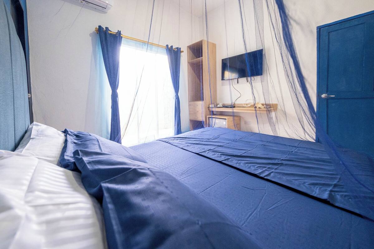 Un dormitorio con cama, cortinas, armario, escritorio y televisor.