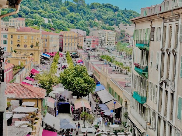 A bustling street with cafes and outdoor seating, surrounded by historic buildings and a hillside in the background.