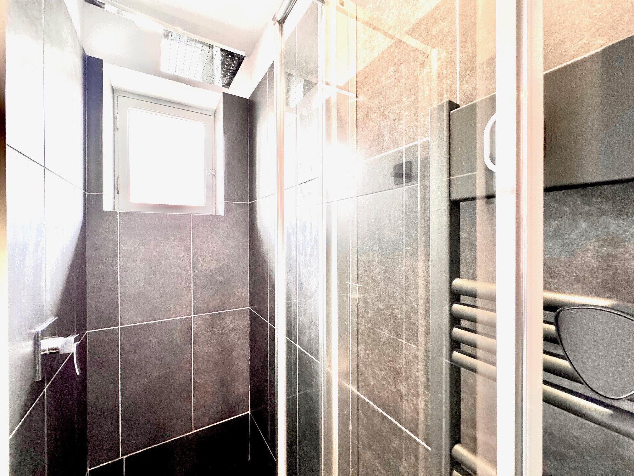 A bathroom with dark tiles, a glass shower enclosure, and a towel rack.