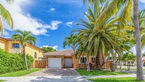 Una casa residenziale con garage, circondata da palme e un prato curato.