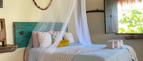 Una cama con dosel, cabecera de madera y ventana con vistas a la vegetación.