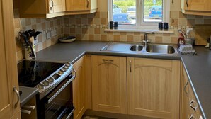 A kitchen with wooden cabinets, a built-in oven, a sink, and a window with a view of the outside. - Peaceful Lakefront Escape w/ Sunset Views (South Cerney)