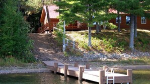 A wooden dock extending into a calm lake, surrounded by trees and a cabin in the background. - Redpebble, a spacious upscale but classic vacation home on a crystal clear lake! (Land O' Lakes)