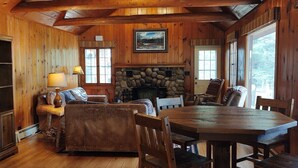 A cozy cabin interior with a stone fireplace, wooden furniture, and large windows. - Redpebble, a spacious upscale but classic vacation home on a crystal clear lake! (Land O' Lakes)