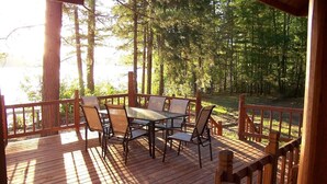 A wooden deck with a table and chairs, surrounded by trees. - Redpebble, a spacious upscale but classic vacation home on a crystal clear lake! (Land O' Lakes)