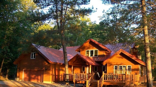 A wooden cabin with a metal roof, a covered porch, and a staircase leading to the entrance. - Redpebble, a spacious upscale but classic vacation home on a crystal clear lake! (Land O' Lakes)