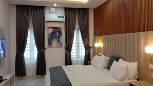 A modern hotel room with a large bed, two bedside tables, a flat-screen TV, and a ceiling light fixture.