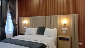 A modern hotel room with a large bed, wooden panel walls, and two bedside tables with lamps.