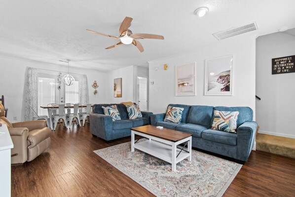 A modern living room with a blue sofa, a wooden coffee table, and a ceiling fan.
