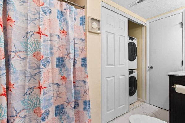 Une salle de bain avec un rideau de douche orné d’un motif représentant la vie marine, une porte blanche et un lave-linge.