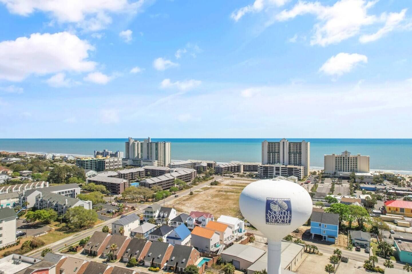 Paisagem costeira urbana com vista clara do oceano, vários edifícios altos e uma torre de água imponente.