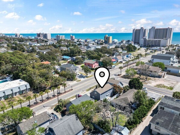 An aerial view of a residential area with a prominent road, houses, and a large body of water in the background.