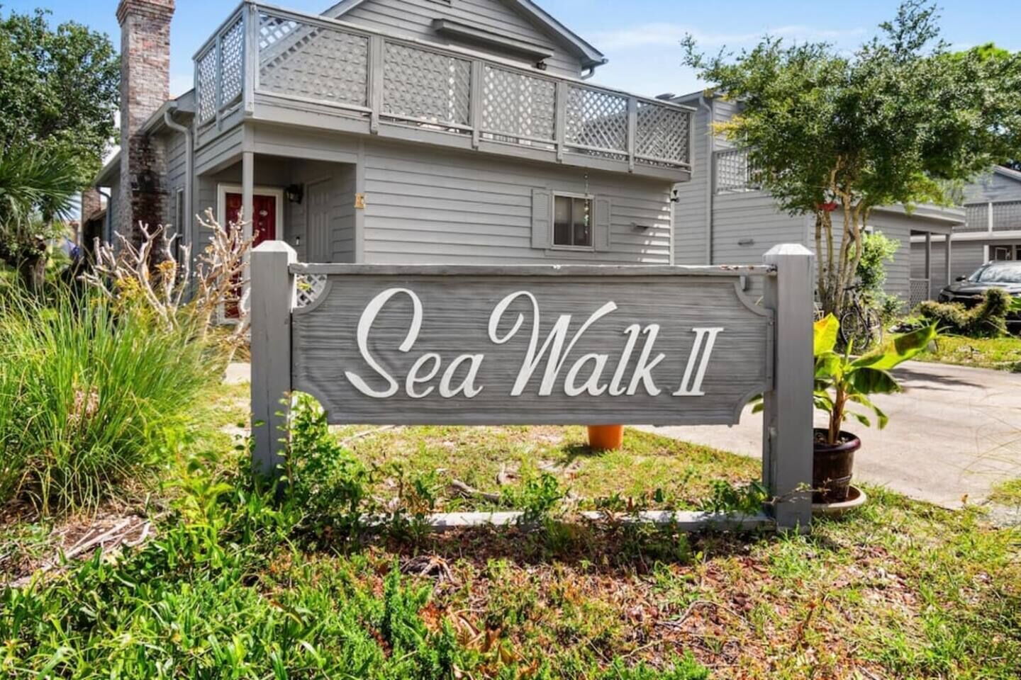 A wooden sign with the text 'Sea Walk II' in front of a house with a balcony.