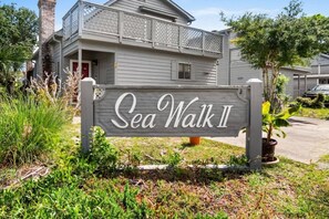 A wooden sign with the text 'Sea Walk II' in front of a house with a balcony.