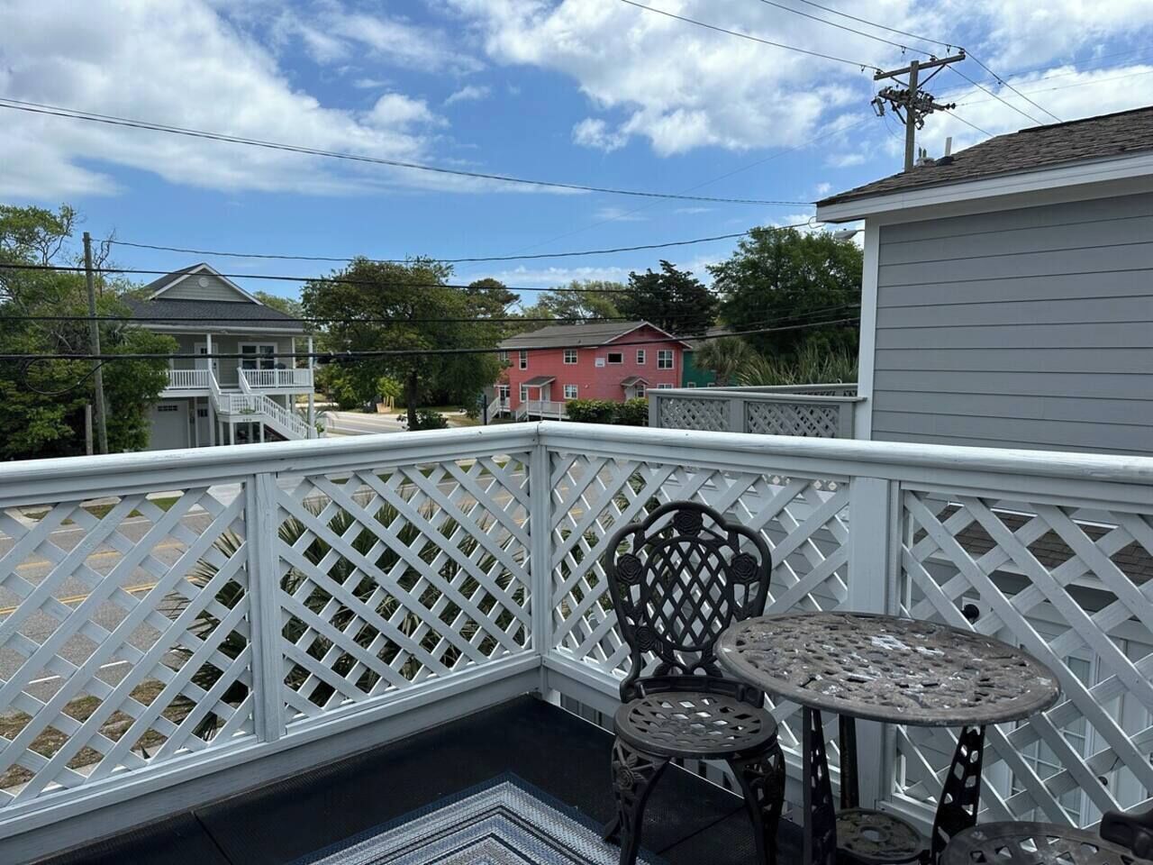 A balcony with a white lattice railing, a round metal table, and a metal chair.