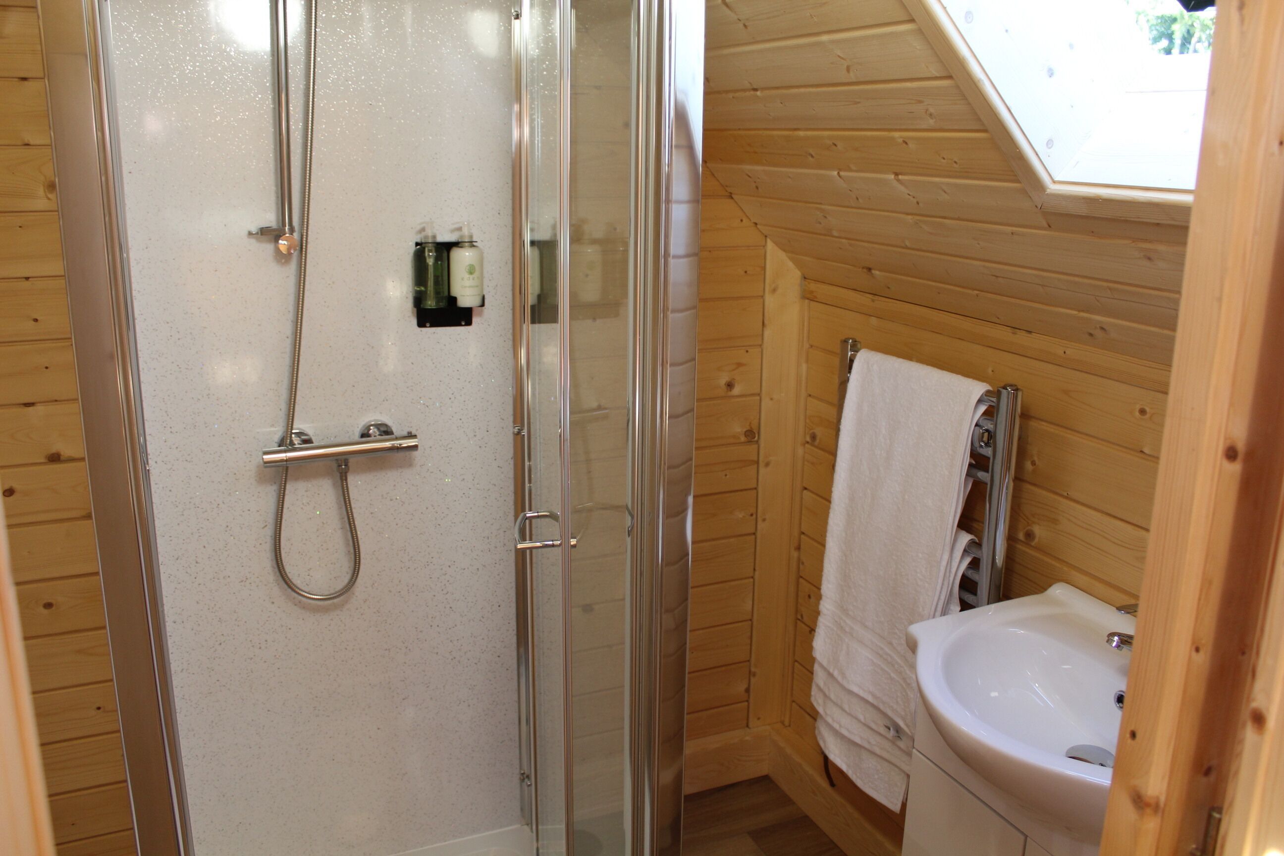 A wooden cabin bathroom with a glass-enclosed shower, a sink, and a towel rack.