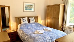 A bedroom with a bed, a wooden wardrobe, a bedside table, a mirror, and a window with curtains. - A beautiful, cosy cottage in a peaceful setting with 15% off ferry (Shanklin)
