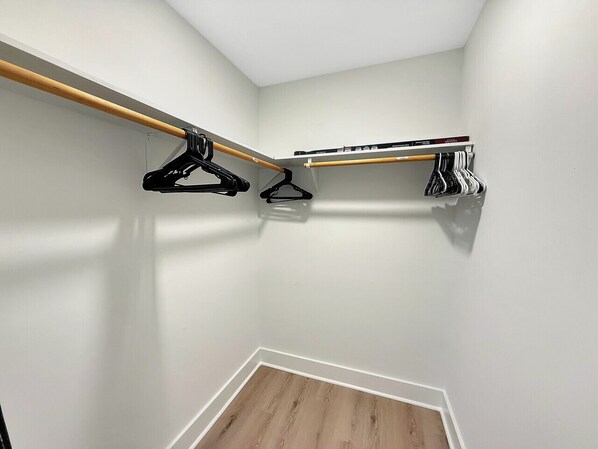 A small, well-lit room with a wooden floor, a white wall, and a built-in closet with a wooden rod and black hangers. - 1BR Garner Gem|Backyard & Pet Friendly (Garner)
