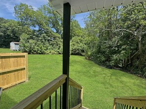 A wooden deck with a railing, surrounded by a well-maintained lawn and dense trees.