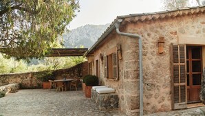 A stone building with a rustic exterior, a stone patio with a table and chairs, and a view of a mountainous landscape. - Can Escu - Villa in the Heart of the Tramuntana Mountains (Sóller)