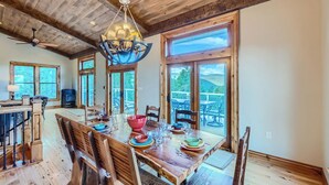 A spacious dining area with a wooden table set for four, large windows, and a view of the outdoors. - Rocky Mountain Retreat - Hot Tub and EPIC views! (Rollinsville)