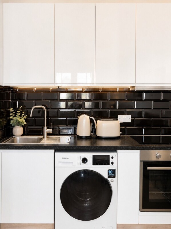 A compact kitchen with a washing machine, a toaster, and a kettle on the countertop.