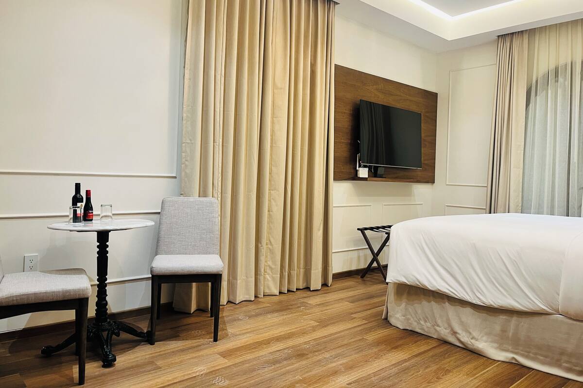 Une chambre d’hôtel avec un lit, un téléviseur fixé au mur, une petite table avec une chaise et une fenêtre avec des rideaux.