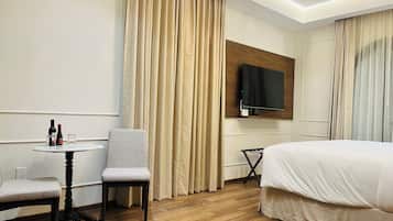 Habitación de hotel con cama, televisión montada en la pared, una mesita con silla y ventana con cortinas.