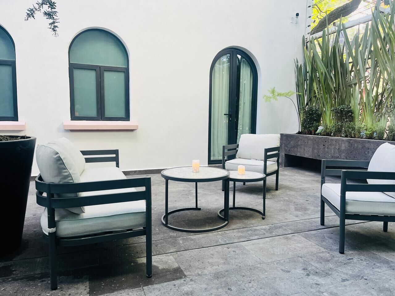Un patio con mobiliario exterior, incluyendo dos sillas y dos mesas redondas, y una maceta grande con plantas.