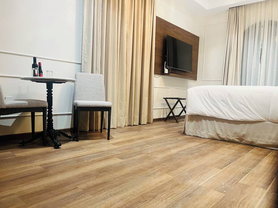 A hotel room with a bed, a chair, a small table, a TV mounted on the wall, and curtains.