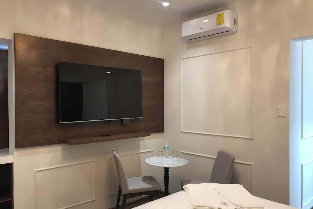 Une chambre d’hôtel équipée d’un téléviseur fixé au mur, d’une petite table ronde avec des chaises, d’un lit recouvert d’une couette blanche et d’un climatiseur mural.
