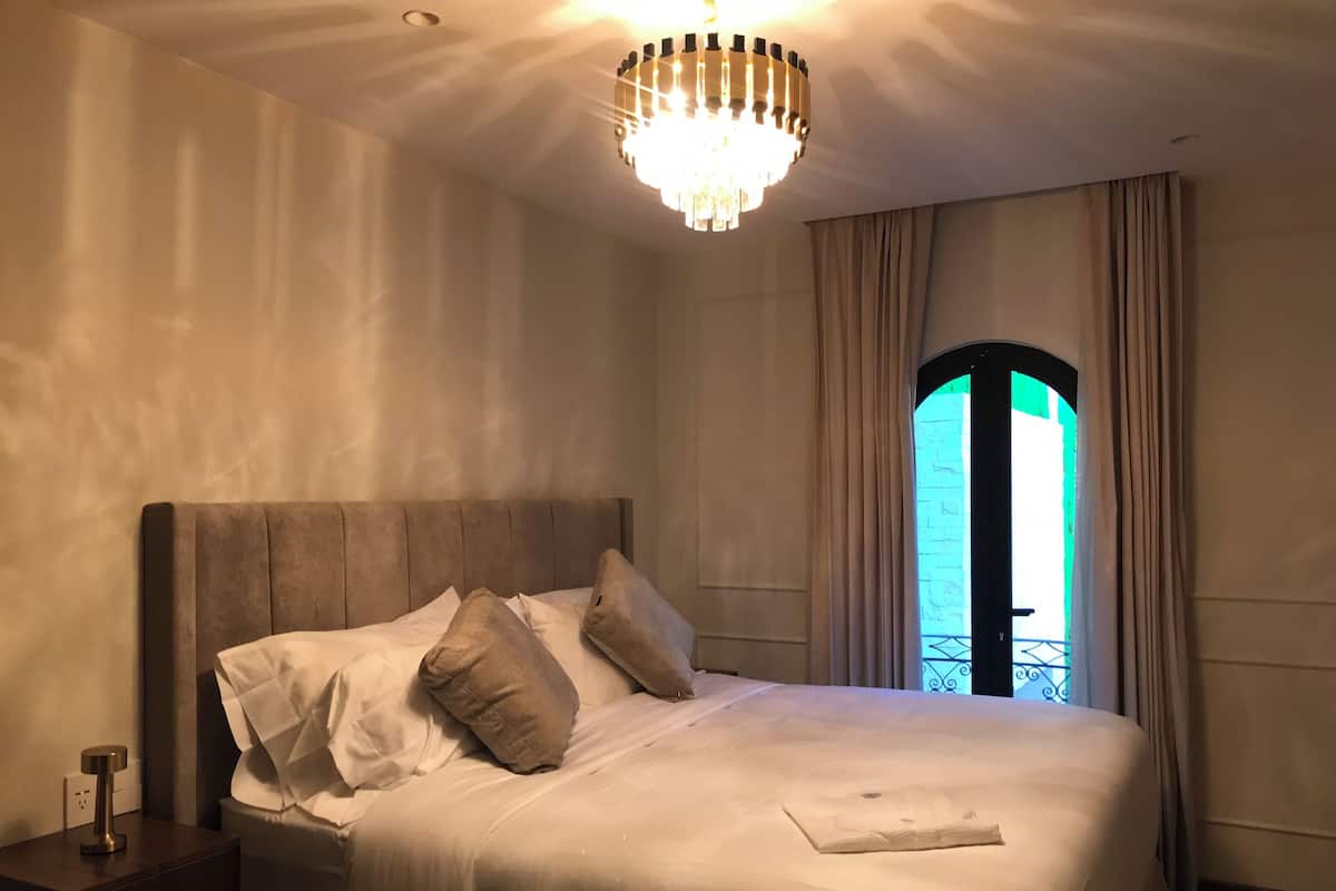 Un lit bien fait, avec une tête de lit, une table de chevet avec une lampe et une fenêtre avec des rideaux.