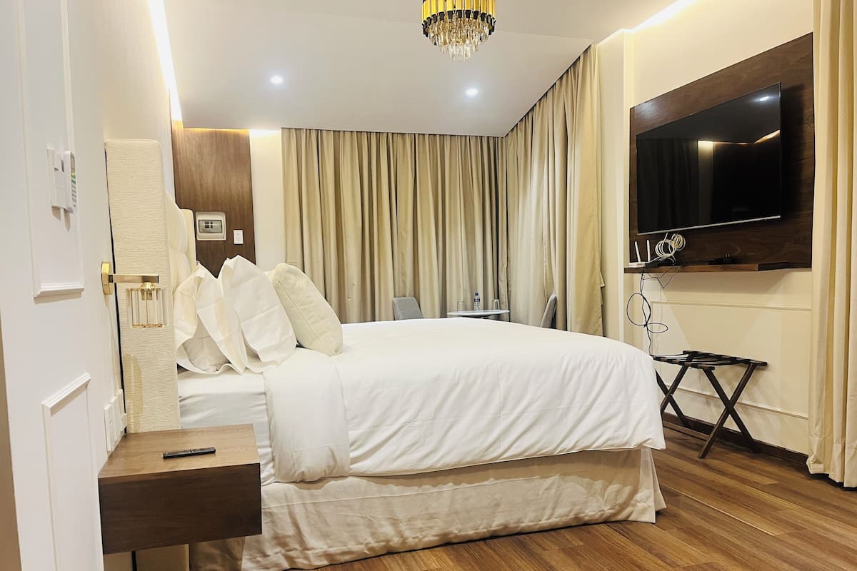 Une chambre d’hôtel avec un grand lit, une table de chevet, un téléviseur à écran plat fixé au mur et un plancher en bois.