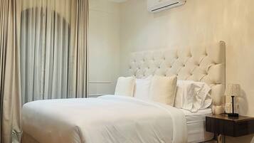 A hotel room with a large bed, a chandelier, an air conditioning unit, and a nightstand with a lamp.