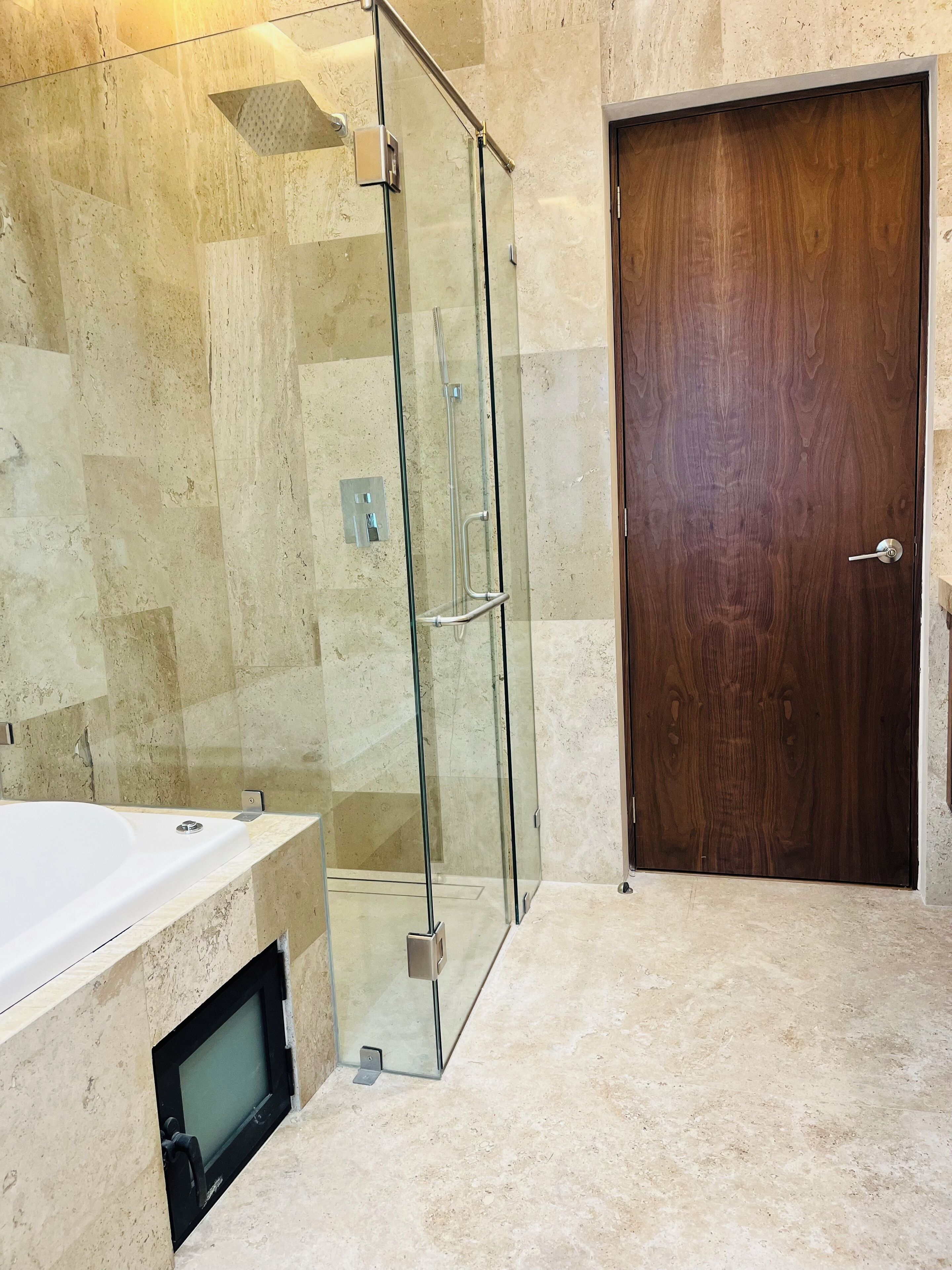 Un baño moderno con ducha envuelta en vidrio, puerta de madera y bañera blanca.
