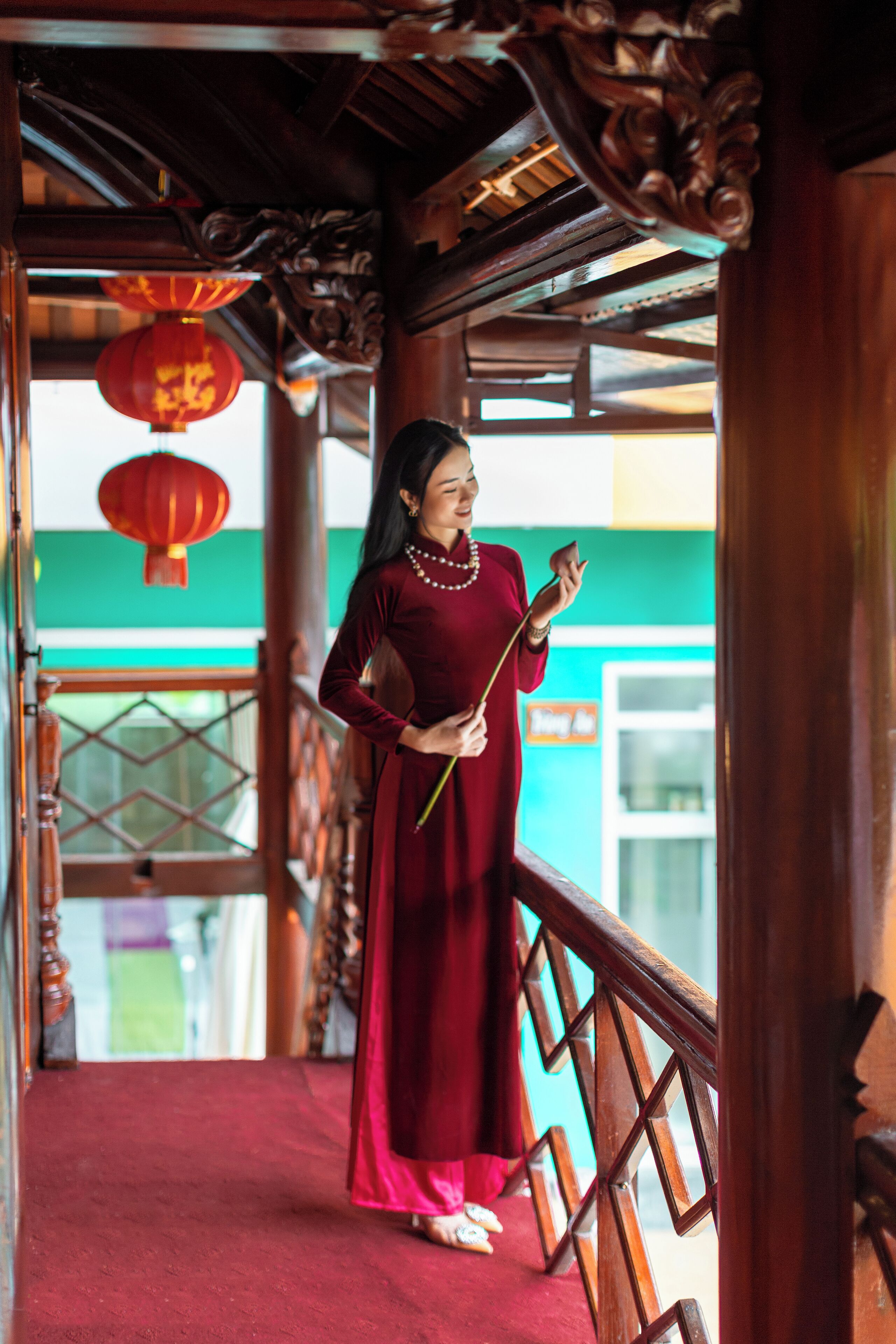 Una persona con vestido rojo parada en una escalera de madera con barandas ornamentales y faroles rojos.