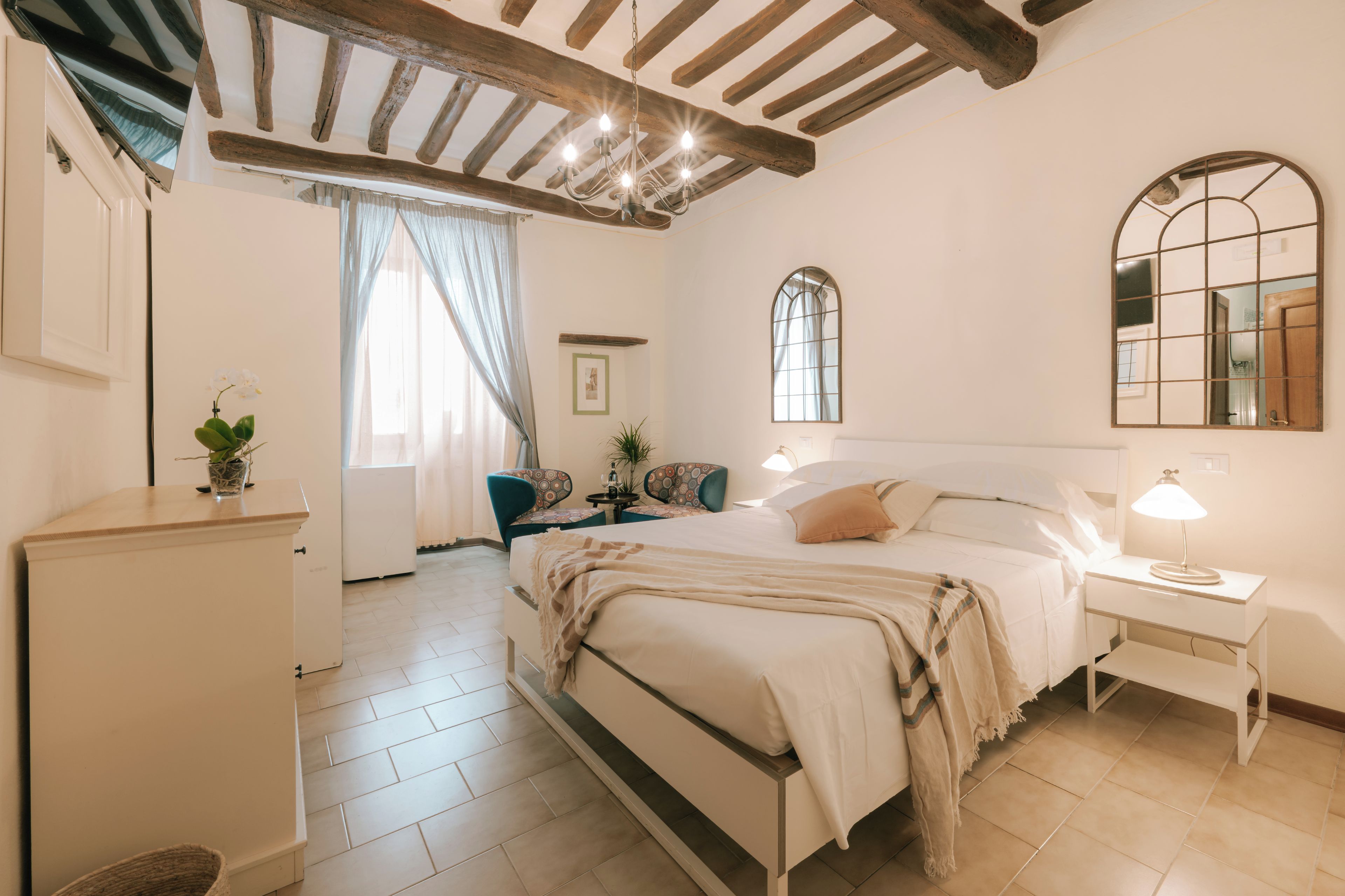 A bedroom with a bed, bedside tables, a mirror, a window, and a ceiling with exposed beams.